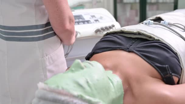 Esthéticienne appliquant masque facial et thérapie de pression corporelle au patient. Jeune femme allongée sur un lit de spa recevant un traitement de beauté complet. — Video