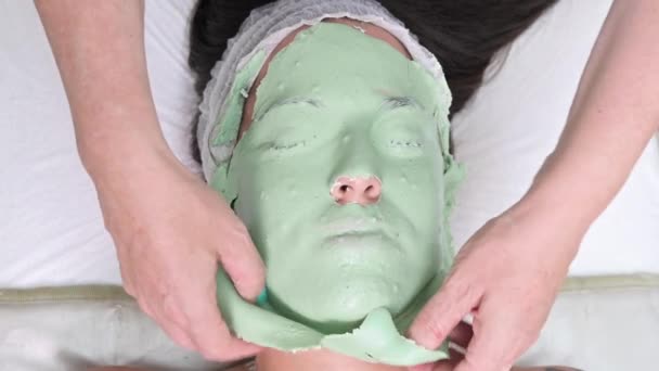 A kozmetikus leveszi a kozmetikai maszkot a fiatal nő arcáról a szépségszalonban. Közelkép — Stock videók