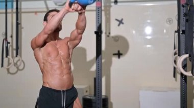 Yakışıklı, kaslı adam ağır bir kettlebell kaldırıyor.