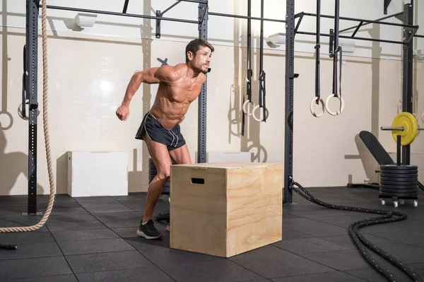 Musculaire mannelijke atleet oefent springen op een houten doos in de moderne health club. Functionele opleiding — Stockfoto