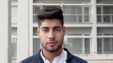 Şirket binasının önünde durup kameraya bakan gülümseyen genç bir adamın portresi..