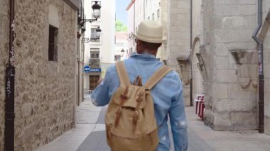 Arka tarafta sırt çantalı genç bir adam var. Eski kasabada sokakta yürüyor..