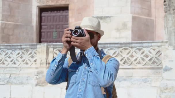 Joven guapo elegante fotógrafo masculino tomando fotos con cámara de fotos al aire libre en el casco antiguo. Hombre alegre haciendo fotos de la arquitectura urbana de la ciudad. — Vídeo de stock