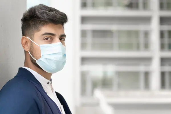 Portrait d'un bel homme en masque médical regardant la caméra à la ville. Beau jeune homme debout dehors dans un masque médical. Concept de coronavirus. — Photo