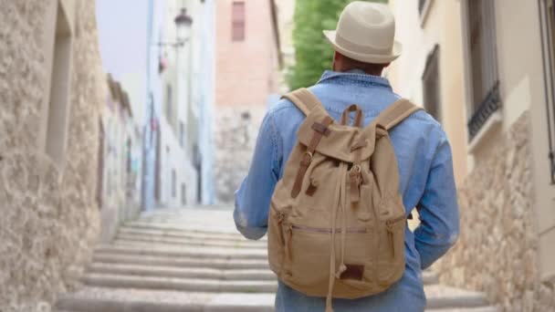 カメラの青いシャツや藁帽子の古代の狭い通りを歩くの観光客に続く 高品質4K映像 — ストック動画