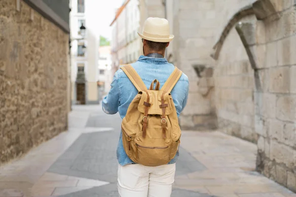 Widok z tyłu młodego człowieka z plecakiem spacerującego po ulicy w starym mieście. — Zdjęcie stockowe