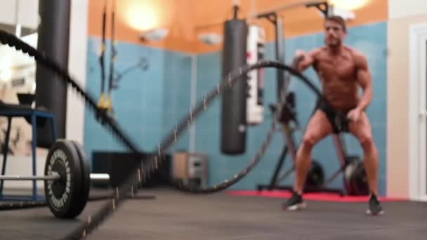 Spierkrachtige man aan het trainen met touw in functionele trainingsfitnessruimte, focus op de voorgrond. — Stockvideo
