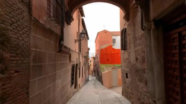 İspanya 'nın Toledo kentindeki dar tarihi ara sokakta iki geleneksel binayı birbirine bağlayan belirgin tuğla kemer bulunuyor. Sıcak dokular, demir balkonlar ve kırsal duvarlar ortaçağ kentsel mimarisinin atmosferik görüntüsünü oluşturur. Yüksek kalite 4k görüntü