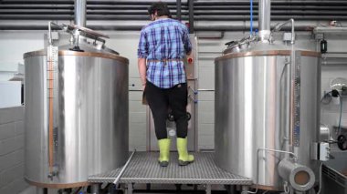 Bira üretim sürecine odaklanmış, modern bira fabrikasındaki büyük paslanmaz çelik tanklar arasındaki otomatik ekipmanı izleyen bir Brewer 'ın yavaş çekim videosu. Yüksek kaliteli FullHD görüntüler