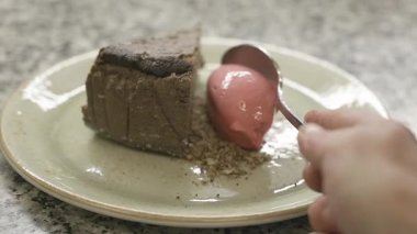 Şef, bir dilim pastanın yanına bir kepçe dondurma ekleyerek tatlıyı kaplıyor ve seramik tabakta zarif bir sunum yapıyor. Yüksek kaliteli FullHD görüntüler