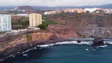 Tenerife 'deki San Juan de la Rambla kıyı şeridi havadan görünüşü, yüksek deniz önü binaları, volkanik kayalıklar ve bulutlu bir gökyüzünün altında Atlantik Okyanusu' nu gösteriyor. Yüksek kalite 4k görüntü