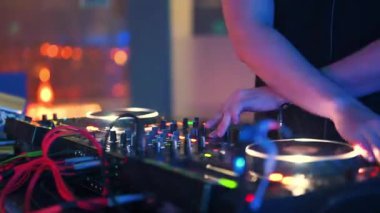 Yakın çekim bir DJ 'in ellerini yakalar profesyonel bir döner tabla kontrolöründe müziği aktif olarak karıştırır, canlı bir parti ya da gece kulübü etkinliği sırasında plağı çizer ve seviyeleri ayarlar. 