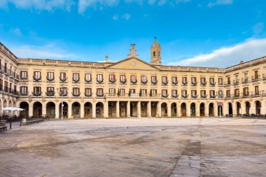 Vitoria-Gasteiz 'deki İspanya meydanının geniş bir görüntüsünde neoklasik cepheler, balkonlar ve parlak mavi bir gündüz vakti gökyüzünün altında açık bir taş meydan yer alıyor. Yüksek kalite fotoğraf