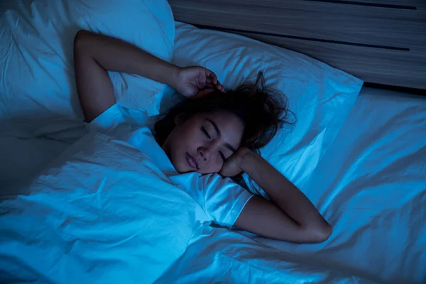 Top View of Beautiful Young Woman Sleeping Cozily on a Bed in His Bedroom at Night. Blue Nightly Colors with Cold Weak Lamppost Light Shining Through the Window.