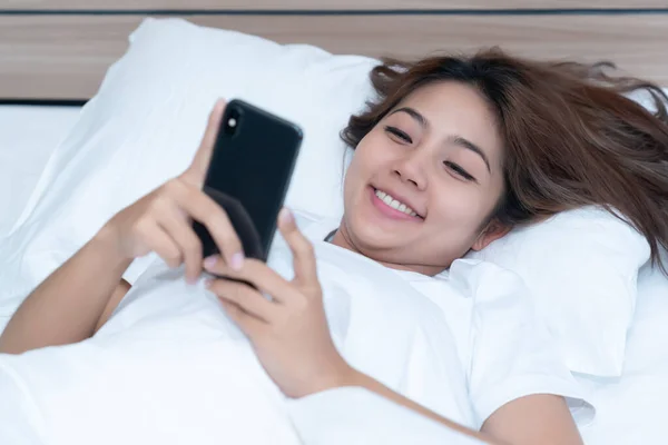 Young asian women lying in bed texting and checking social apps in smartphone on bed before after she sleeping at night. Mobile addict concept.