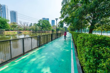 Çocuklar ve yetişkinler şehir ve bina yakınlarındaki parkta bisiklet sürerken rahatlar ve mutlu olurlar.. 