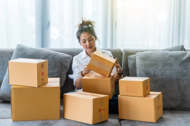 Kanepede oturan güzel Asyalı kadınlar küçük işletmelerle dolu bir sürü paket kutusuyla online alışveriş yapan müşterilere satıyorlar. İnternet üzerinden satış ve alışveriş kavramı
