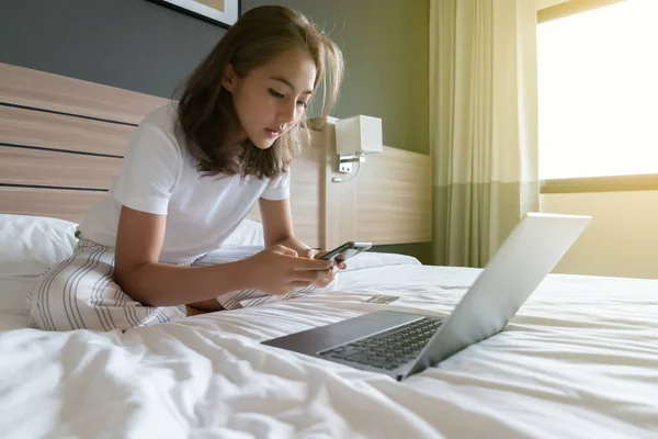 Smiling woman lying down the bed and her laptop. She is on the phone to talk about work. WFH Working from home in quarantine lockdown. Social distancing Self Isolation