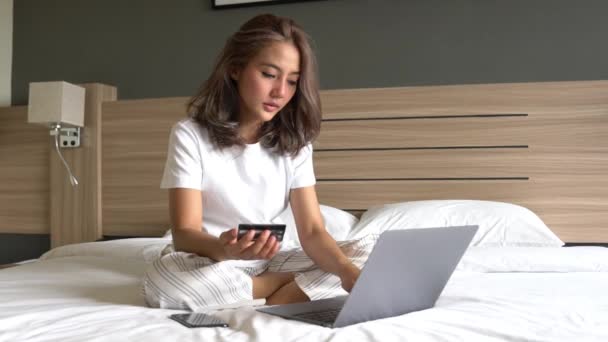 ラップトップとクレジットカードでベッドの上の美しいアジアの女性は 彼女はオンラインで買い物 公共料金を支払う 午前中にチケットを購入する 朝はオンラインショッピングのための時間をリラックス — ストック動画