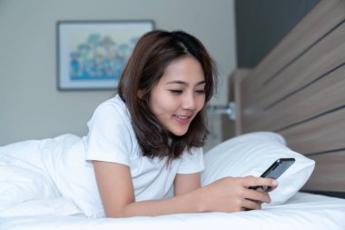 Genç Asyalı kadınlar, geceleri uyuduktan sonra yataktaki akıllı telefonlarda mesajlaşıp sosyal uygulamaları kontrol ediyorlar. Mobil bağımlılık kavramı.