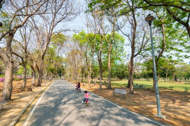 Çocuklar ve yetişkinler şehir ve bina yakınlarındaki parkta bisiklet sürerken rahatlar ve mutlu olurlar.. 