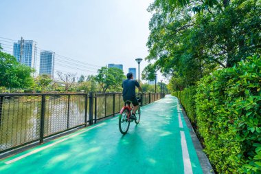 Çocuklar ve yetişkinler şehir ve bina yakınlarındaki parkta bisiklet sürerken rahatlar ve mutlu olurlar.. 