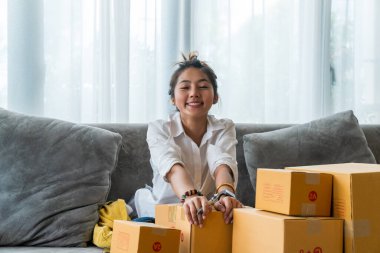 Kanepede oturan güzel Asyalı kadınlar küçük işletmelerle dolu bir sürü paket kutusuyla online alışveriş yapan müşterilere satıyorlar. İnternet üzerinden satış ve alışveriş kavramı