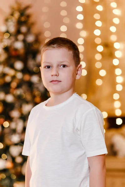 白いTシャツを着た8歳の男の子がクリスマスを背景にカメラを見る — ストック写真