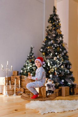 Pijamalı ve Noel Baba şapkalı bir çocuk Noel için tahta bir ata biner.