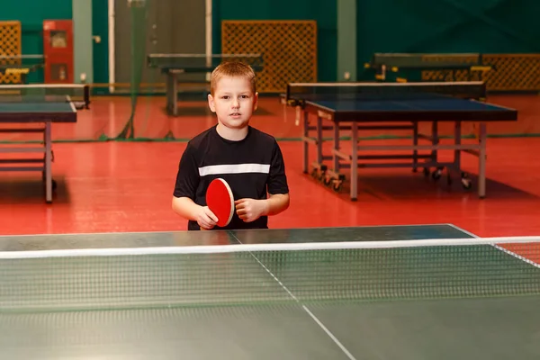 an eight-year-old boy in a black T-shirt plays table tennis. racket in hand