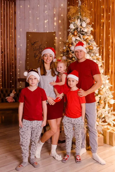 a family of five stands near the Christmas tree. family photo shoot. vertical photo