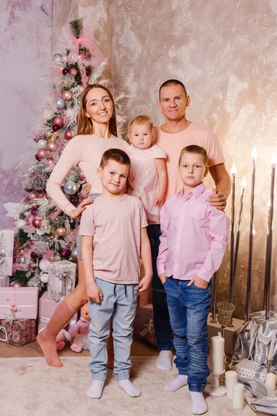 stylish family of five in delicately pink clothes near the Christmas tree. family photo shoot. vertical photo three children and parents
