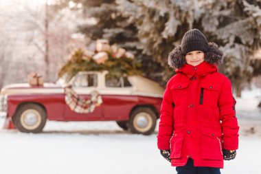 Sevimli, yedi yaşında, kırmızı ceketli bir çocuk kışın kameraya bakar.