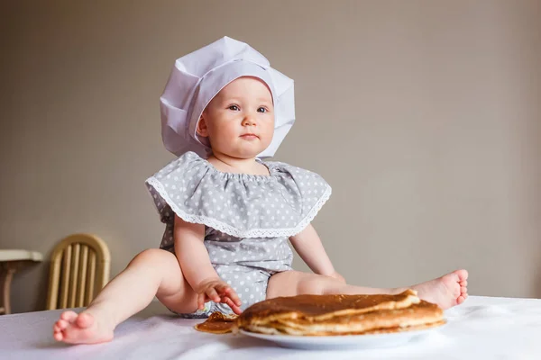 photo shoot of a little girl in a white cook\'s cap at home in the kitchen. Russian Carnival