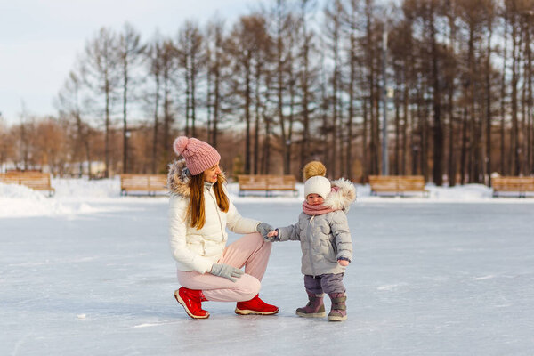 Счастливая молодая женщина и полуторагодовалая девочка зимой в теплых куртках прогуливаются по парку. мать и дочь в зимней одежде.