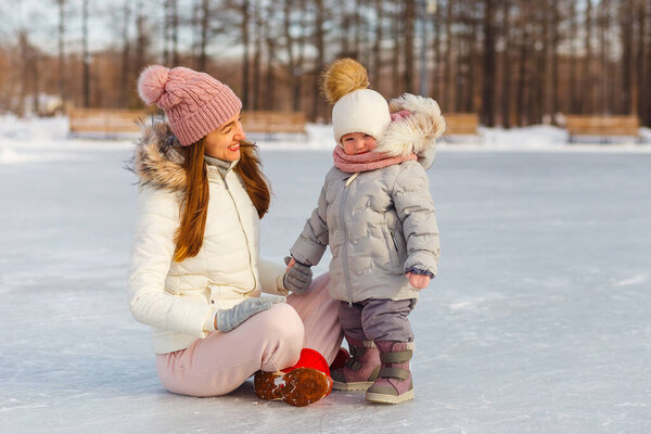 Счастливая молодая женщина и полуторагодовалая девочка зимой в теплых куртках прогуливаются по парку. мать и дочь в зимней одежде.