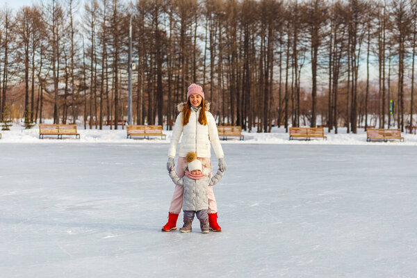 Happy young woman and one-and-a-half-year-old girl in winter in warm jackets walk in the park. mother and daughter in winter clothes.