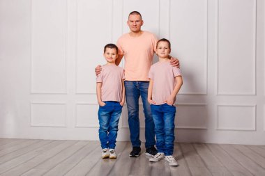 Mutlu baba içeride kot giymiş iki oğlana sarılıyor.