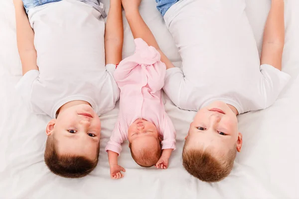 three children lie on their backs on a white sheet. Two older brothers and a newborn baby girl
