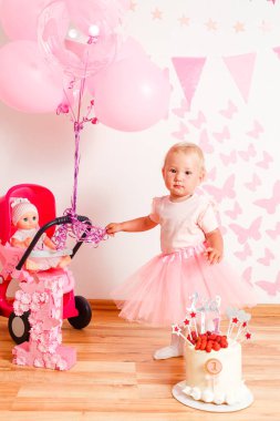 Bir yıl sonra küçük bir kıza doğum gününü kutluyoruz. Çilekli beyaz pasta, pembe süslemeli kelebekler ve toplar.