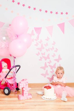 Bir yaşındaki bir kız çocuğu doğum günü için büyük beyaz bir pastayla el kırıyor.