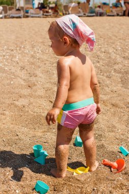 Bir yaşında bronzlaşmış bir kız çocuğu yazın kumsalda sırtı dönük durur.