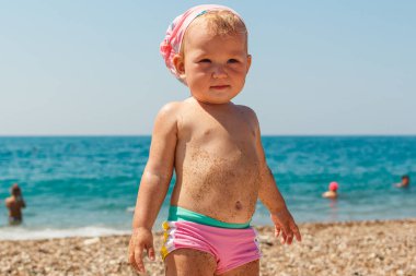 Bandanalı sevimli bir kız kumsalda duruyor.