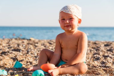 Bir yaşındaki kız yazın kumsalda kumla oynuyor.