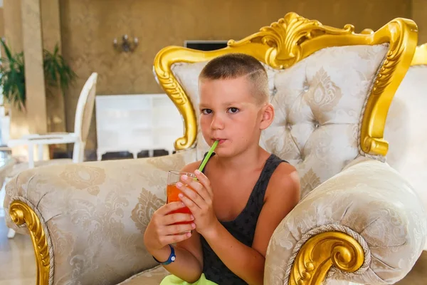 男の子が椅子に座り ホテルでフルーツジュースを飲む — ストック写真