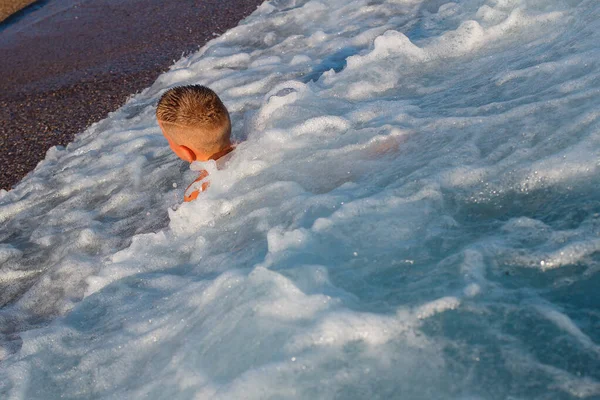 9歳の少年が波に乗って浜辺に横たわっています — ストック写真