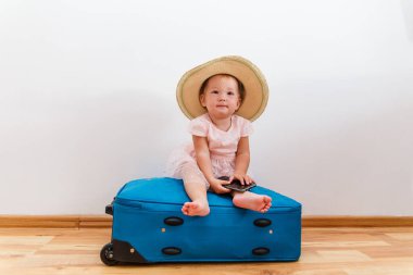 Hasır şapkalı, elinde telefonla içeride büyük bir bavula oturan sevimli bir kız.