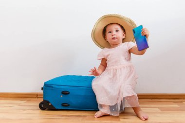 Hasır şapkalı, elinde telefonla içeride büyük bir bavula oturan sevimli bir kız.