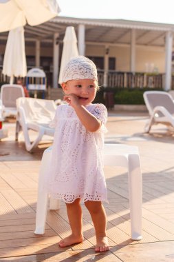 Beyaz eşarplı, bronz tenli tatlı bir kız yazın güneşin altında otel bahçesinde çıplak ayakla duruyor.