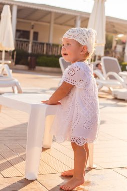 Beyaz eşarplı, bronz tenli tatlı bir kız yazın güneşin altında otel bahçesinde çıplak ayakla duruyor.